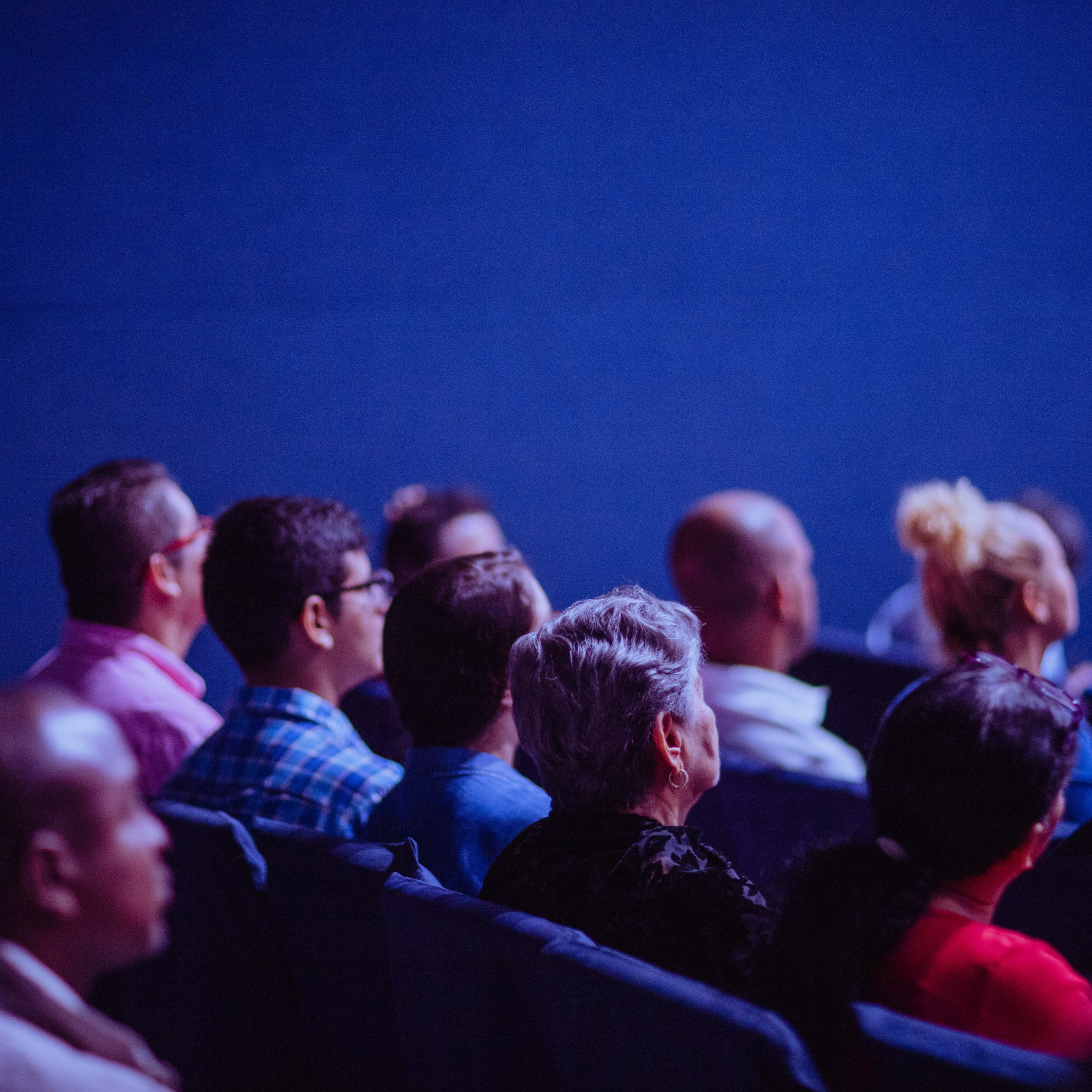 Audience seated in a blue-lit auditorium  watching a film.